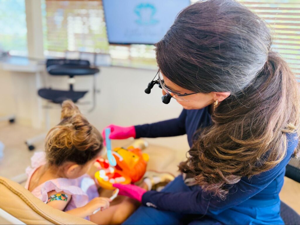 Dr. Mary Margaret Kratz teaching proper brushing to a young patient using a toy model at Little Pearls Pediatric Dentistry in St. Louis.